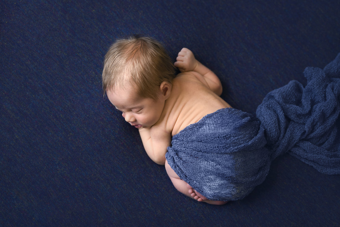 newborn baby boy curled up on blue blanket