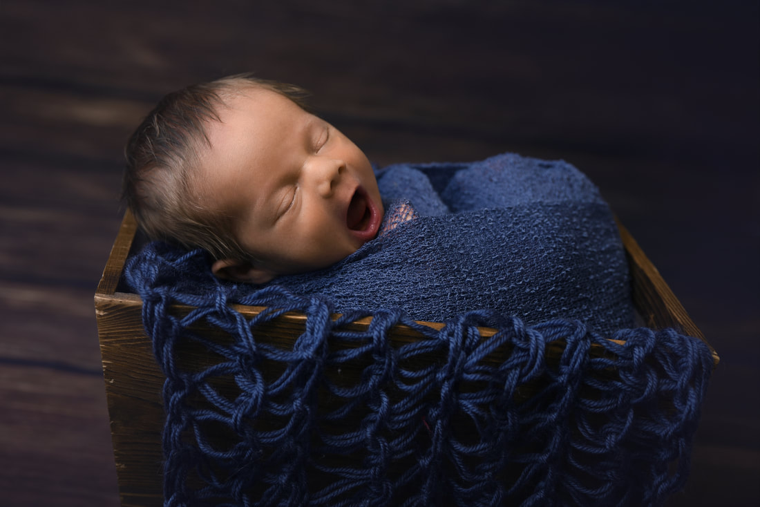 yawning newborn baby boy wrapped in blue